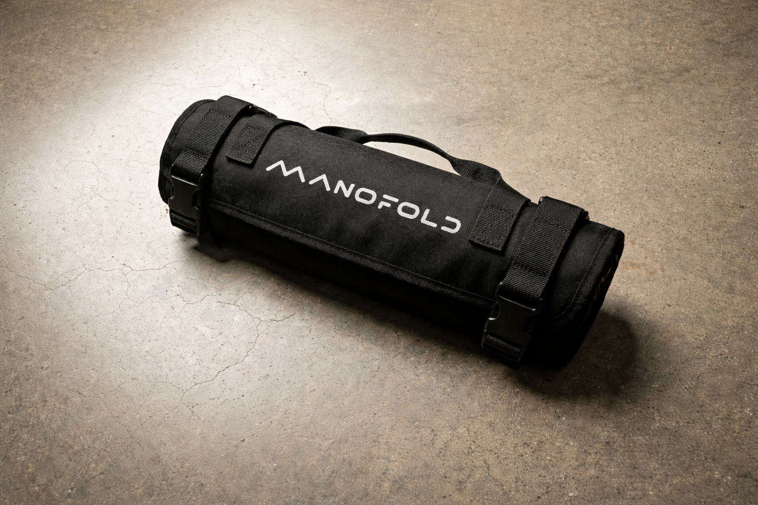 Black roll-up bag with 'Manofold' branding on a beige surface