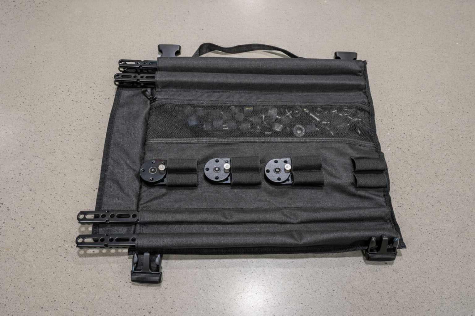 Black tactical pouch with various components on a gray surface